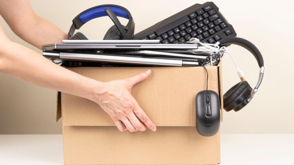 Woman hands holding cardboard box full old used computers, phones, tablets, gadget devices for recycling. Planned obsolescence, e-waste, donation, electronic waste for reuse and recycle concept